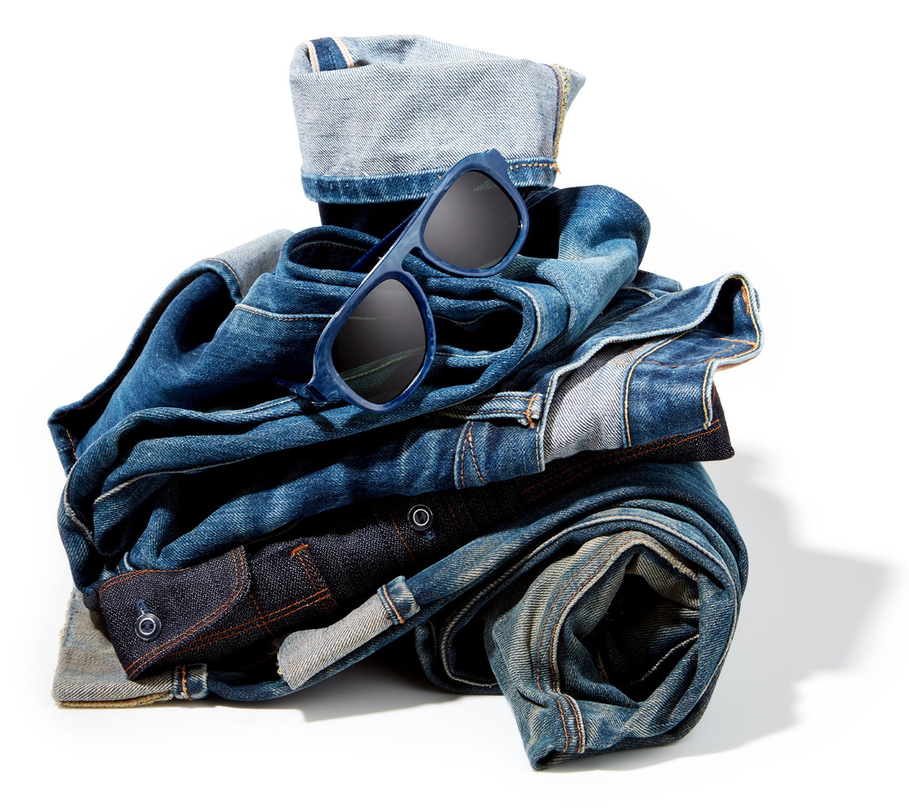 Stack of denim jeans with sunglasses on a white background