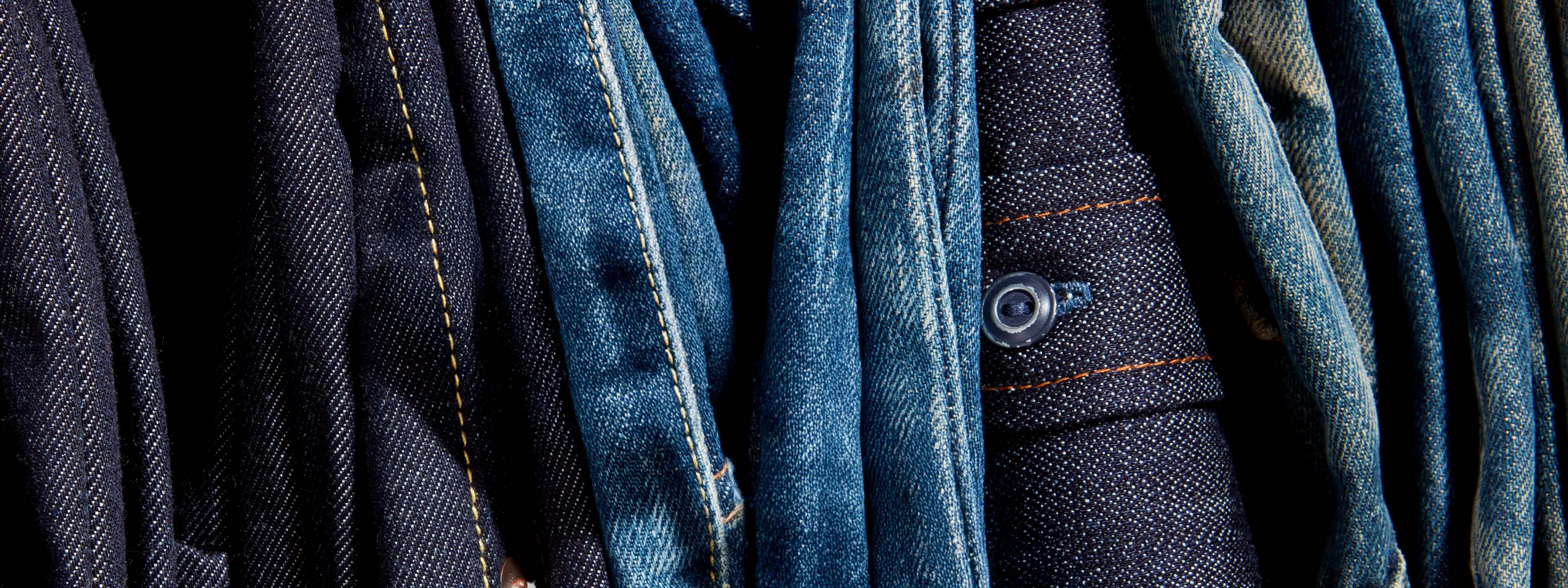 Stack of blue jeans with various shades and textures.