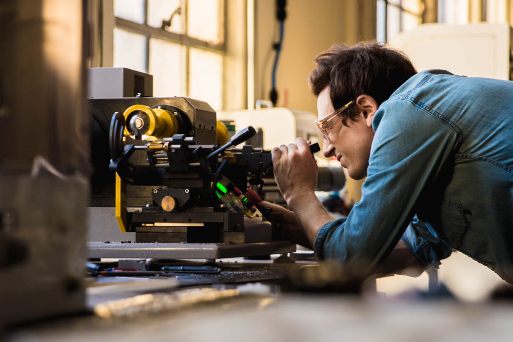 A worker is squinting while carefully handling a machine.
