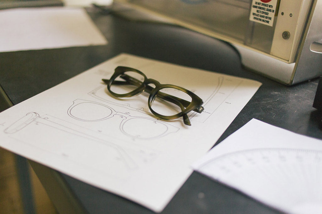 A pair of Lowercase optical frames lay on top of a technical drawing of the very same frame.