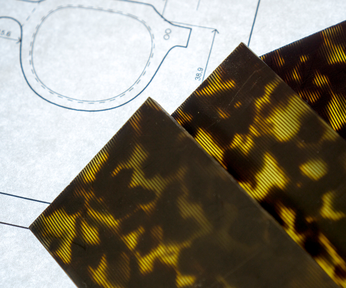 Sheets of tortoise acetate lay on top of technical drawings of optical frames.